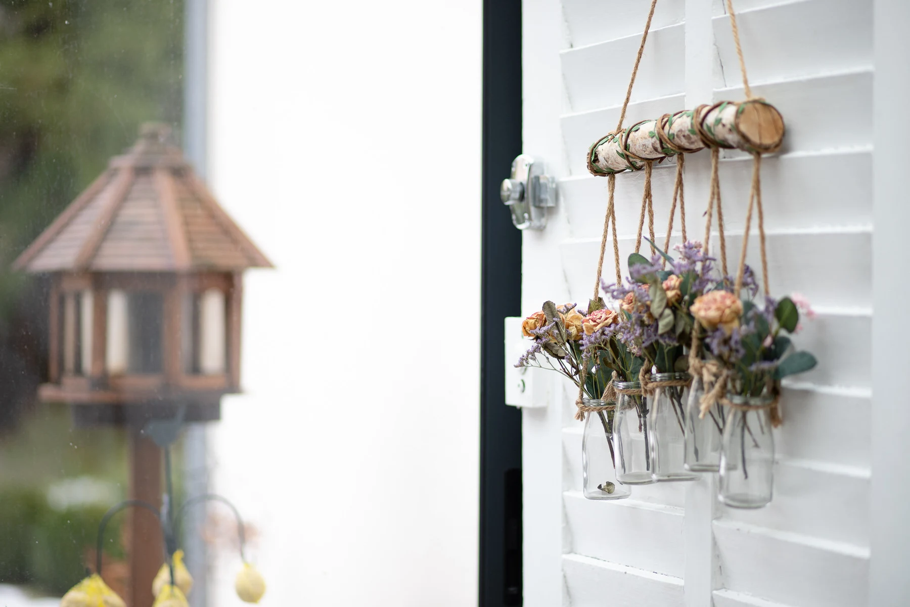 Vases de fleurs séchées suspendus à un volet blanc, gazebo en arrière-plan dans le jardin