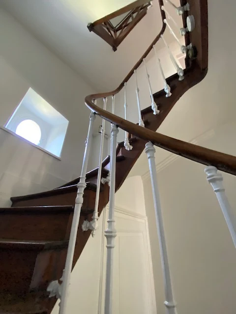 L'escalier vu d'en haut : rampe en bois, balustres blancs et œil-de-bœuf