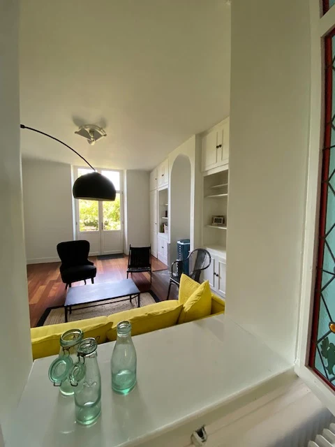 Le salon vu depuis l'entrée : canapé jaune, fauteuils noirs et vitrail au-dessus du passage