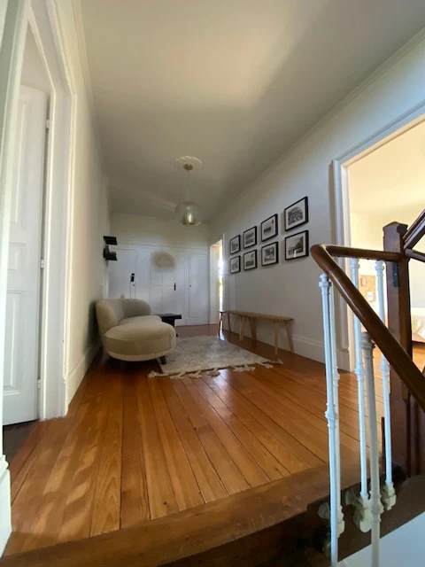 Le palier du premier étage : parquet, banc en bois et photos anciennes encadrées