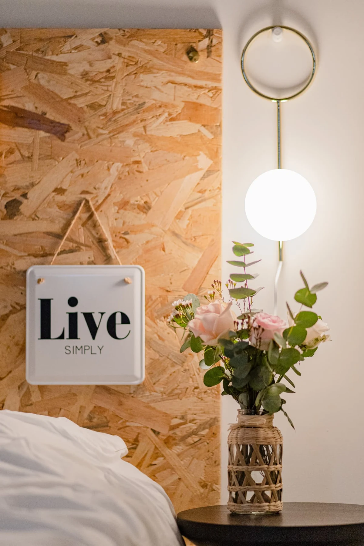 Tête de lit en bois d'atelier avec pancarte « Live Simply », bouquet de roses et lampe annulaire