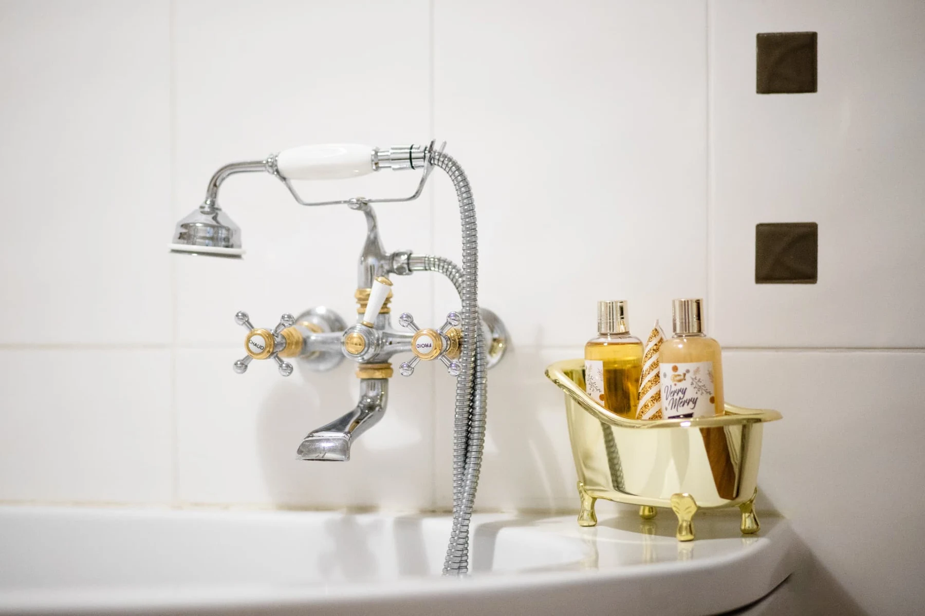 Robinetterie ancienne chromée de la baignoire et petite baignoire dorée remplie de savons