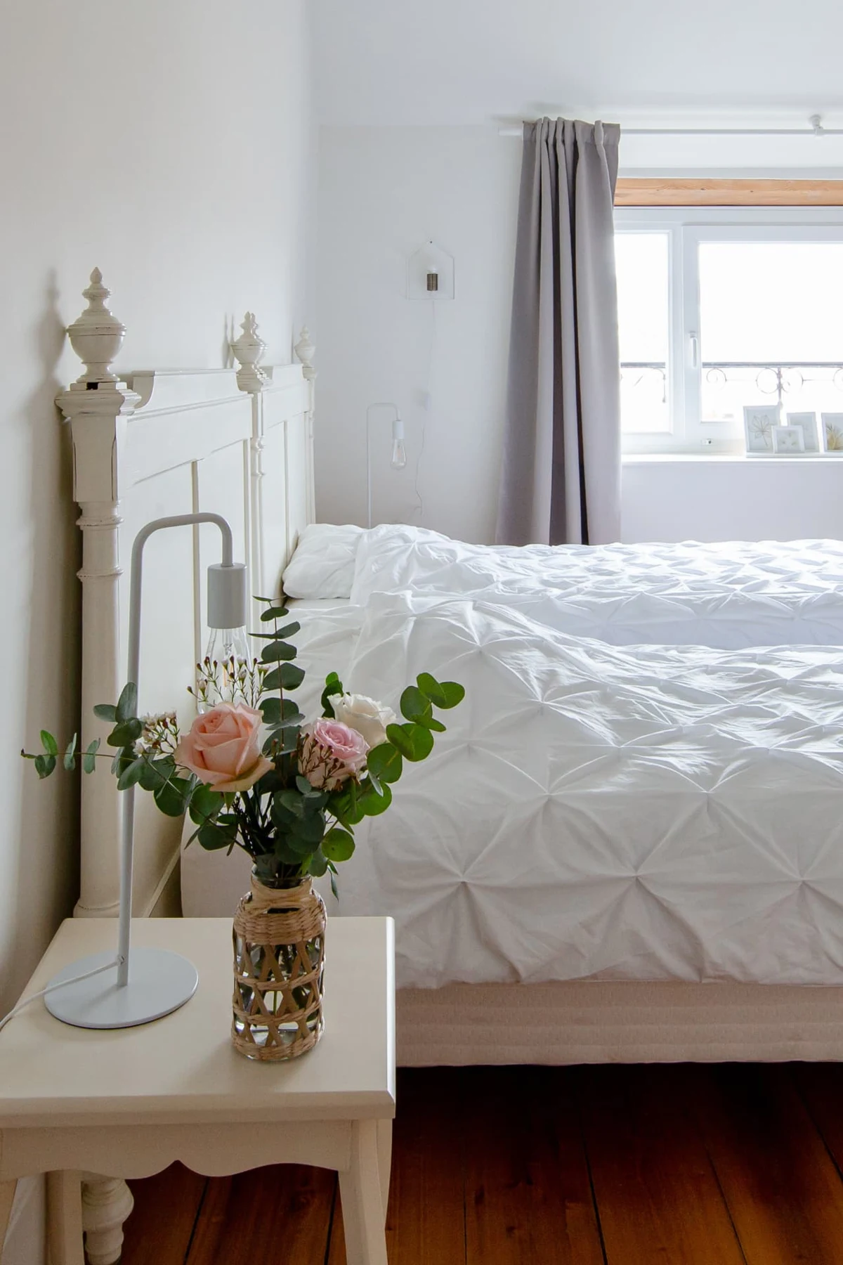 Chambre blanche : lit à tête ouvragée, chevet fleuri de roses et d'eucalyptus