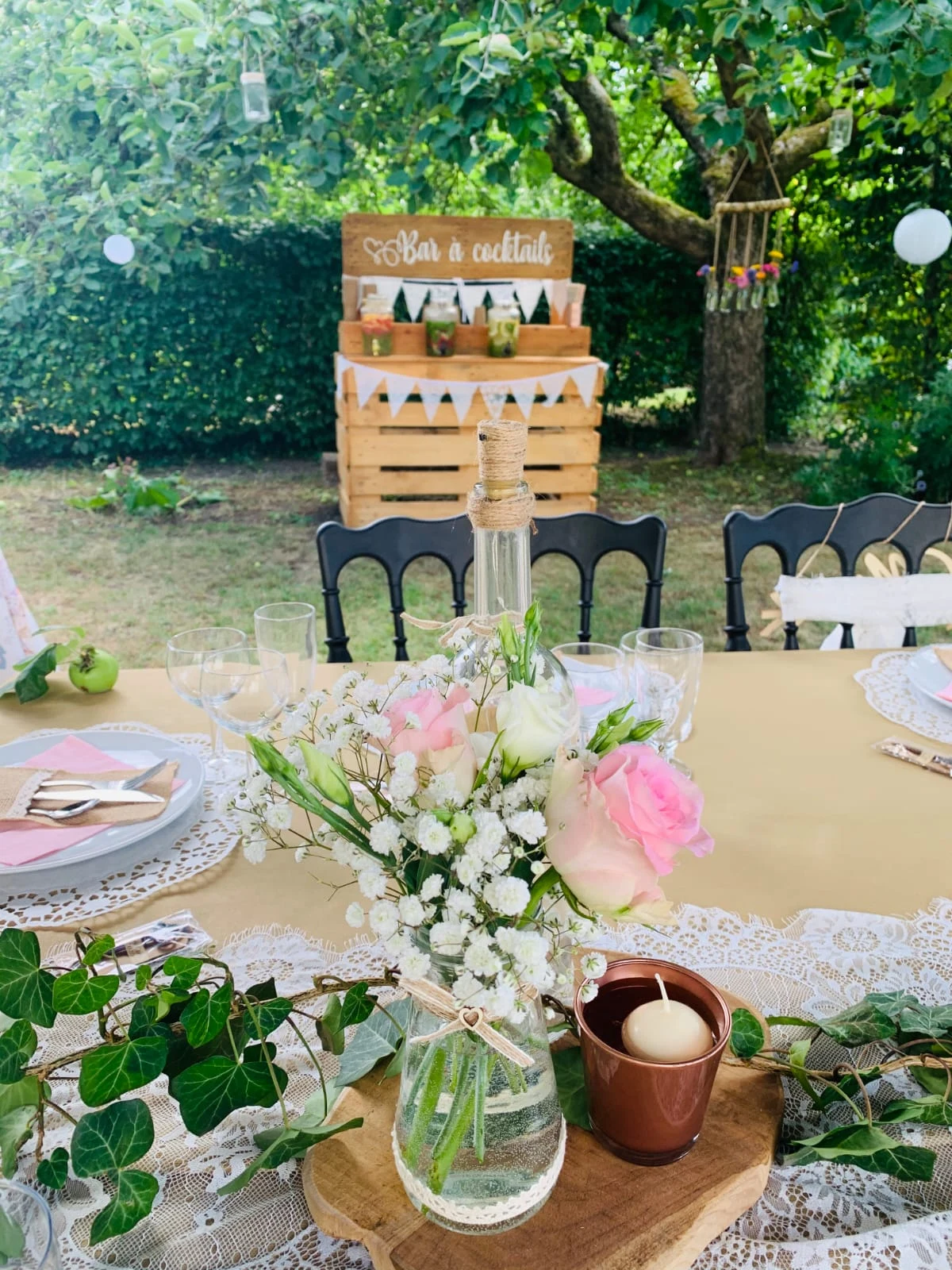 Table de fête dressée dans le jardin devant le bar à cocktails en palettes, guirlandes et lampions