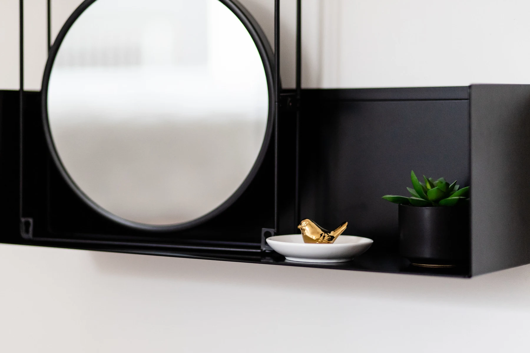 Étagère noire : miroir rond, petit oiseau doré sur coupelle et succulente