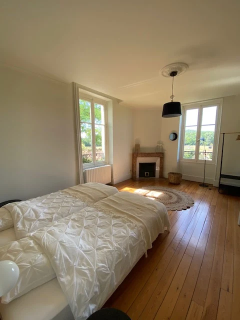 Chambre aux deux fenêtres : grand lit blanc, parquet clair et vue sur le jardin