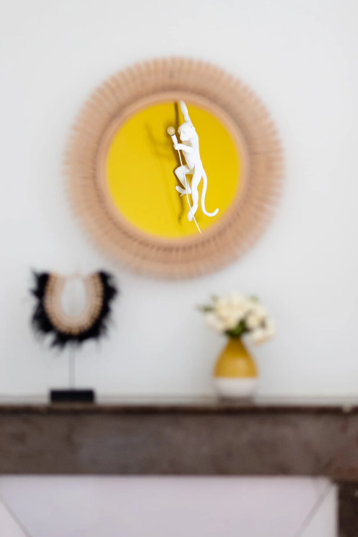 Lampe singe blanc grimpant sur un médaillon jaune à franges, au-dessus de la cheminée