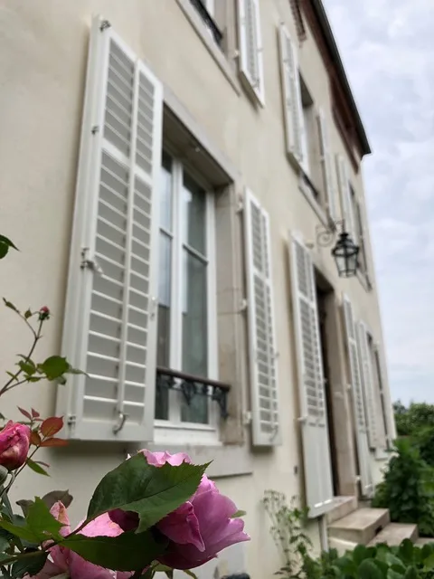 Volets clairs et rosier en fleurs le long de la façade