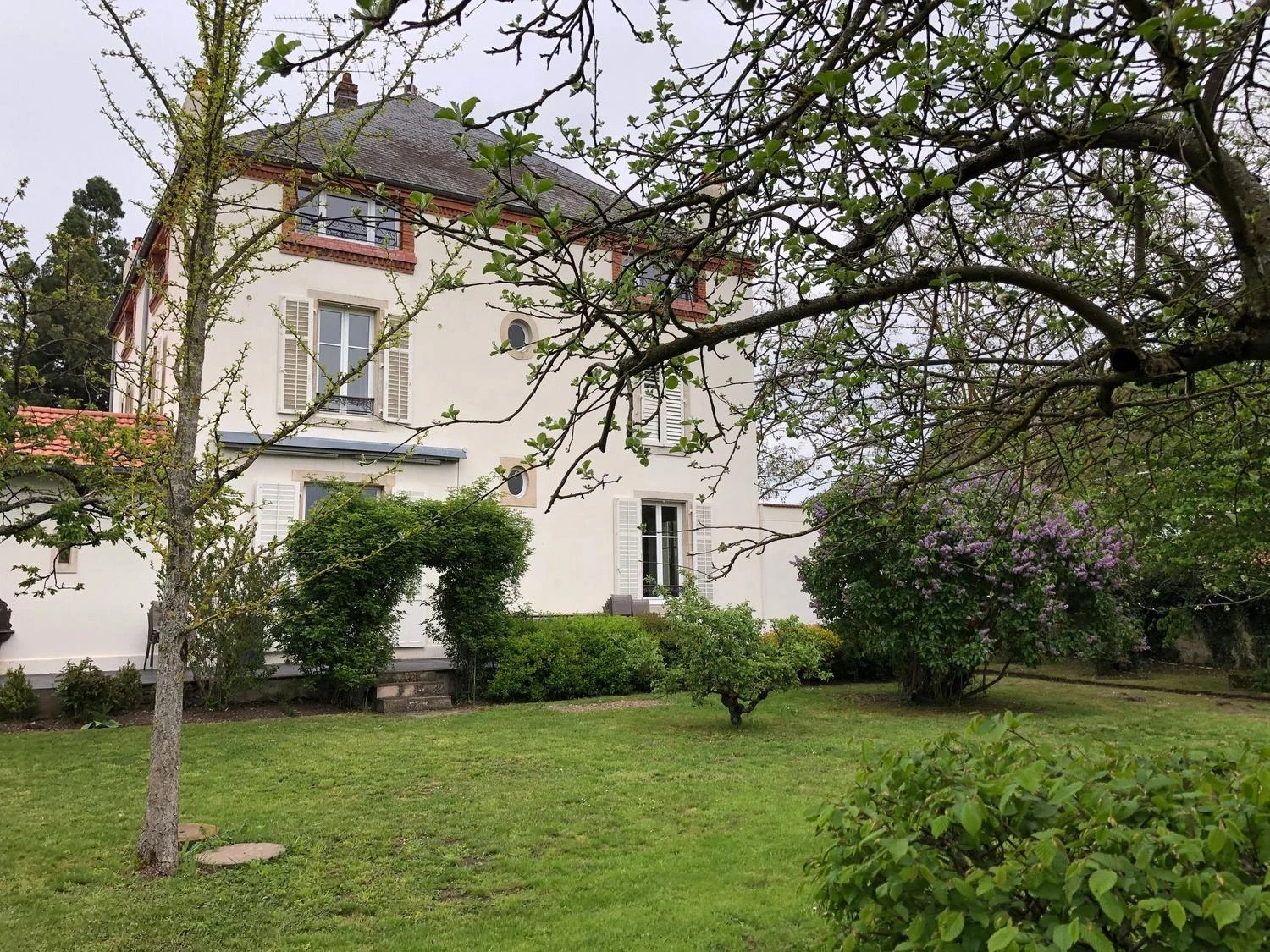La Maison 1881 vue du jardin au printemps, lilas en fleurs et pelouse