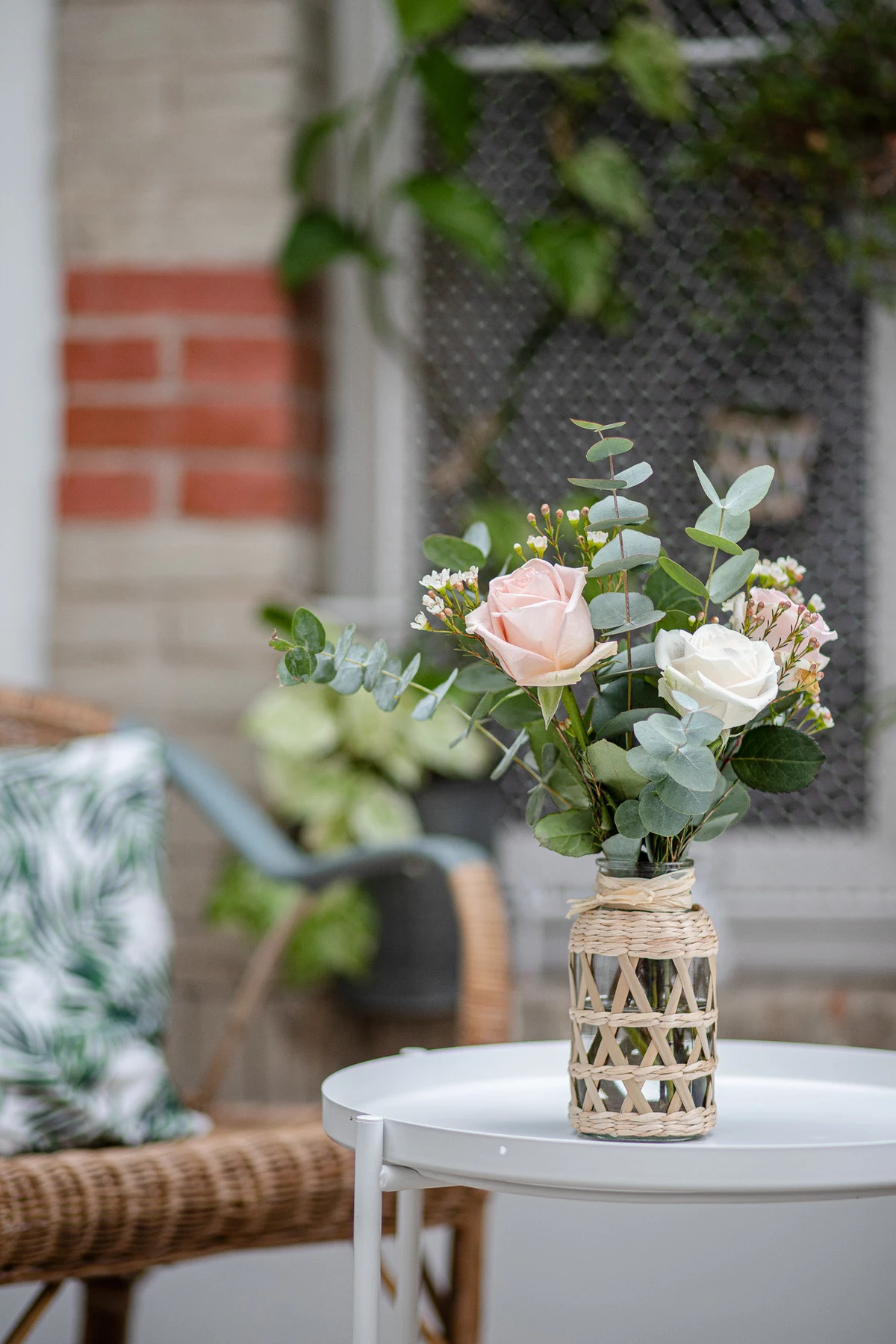 Bouquet de roses pâles et d'eucalyptus dans un vase tressé, posé sur une table blanche